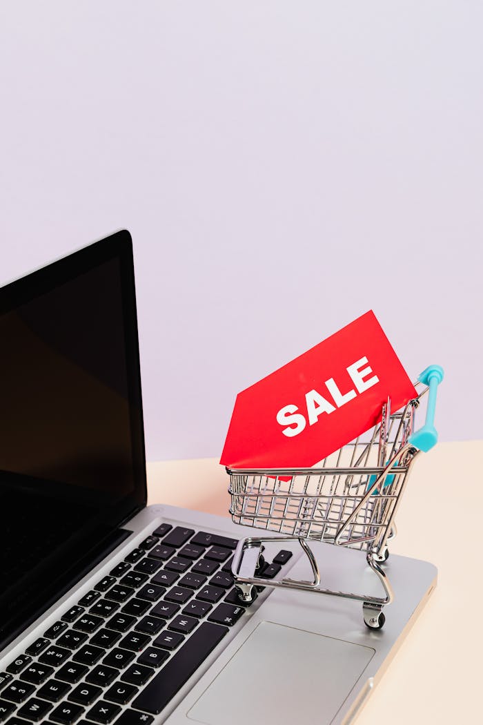 A Red Sale Tag on a Miniature Shopping Cart Placed on a Macbook Laptop